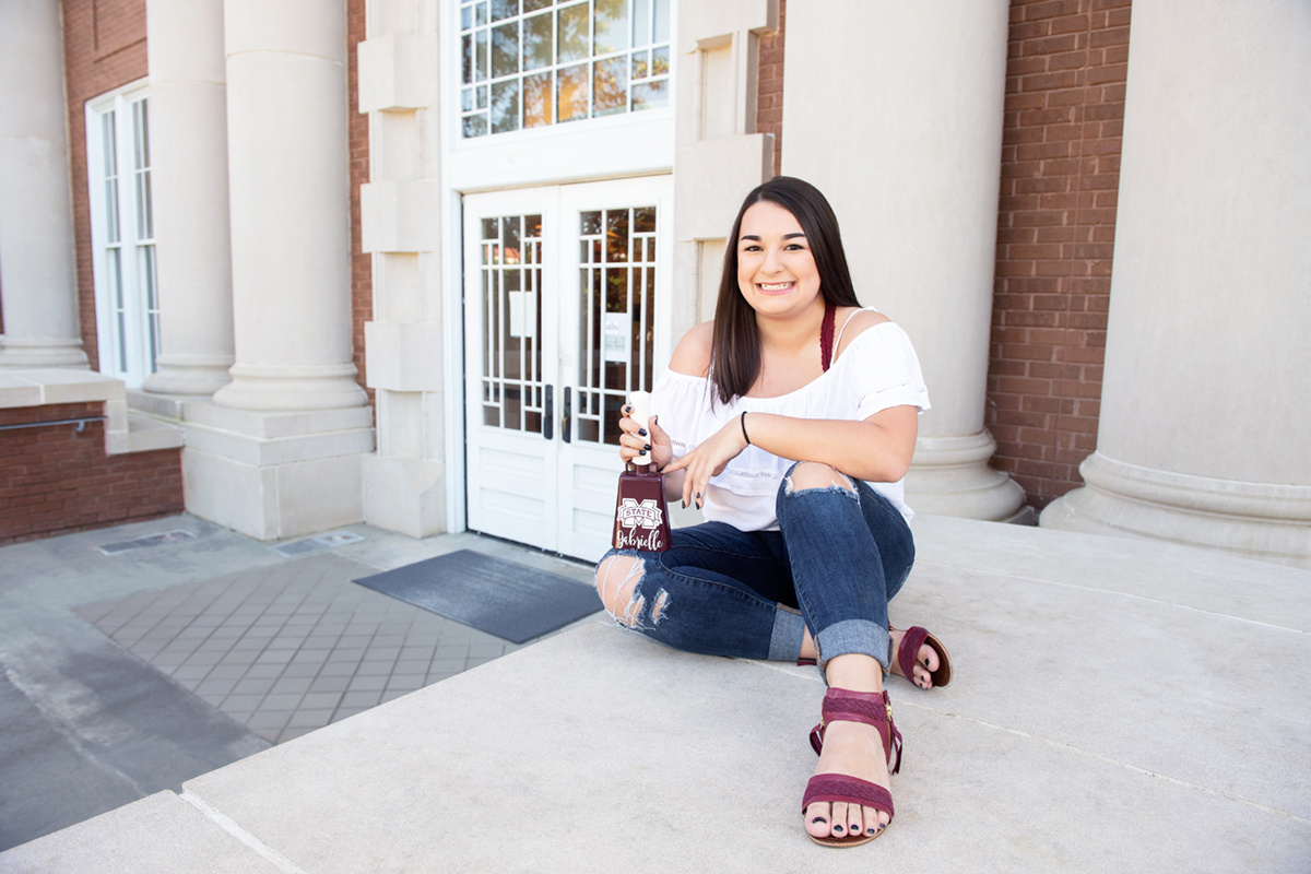 Gabrielle Heckler, pictured in front of Lee Hall holding a cowbell.