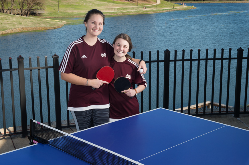 Amelia Andersson and Rebecca Siciliano pose by a ping pong table with Chadwick Lake in the background.