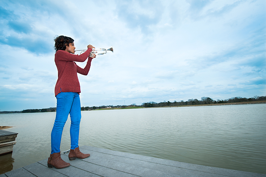 Makayla Brister plays a trumpet on the banks of a lake.