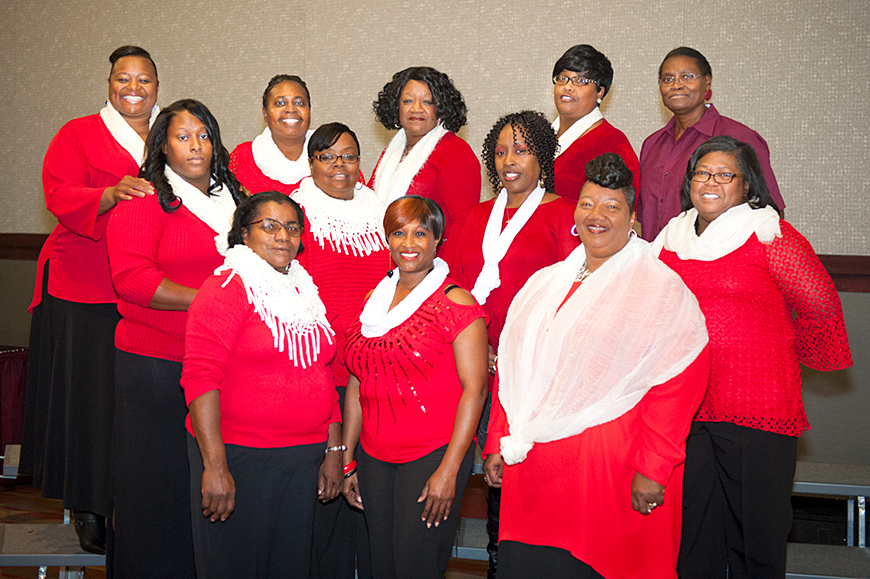 The MSU Custodial Choir, pictured at a Christmas party wearing red shirts and white scarves.