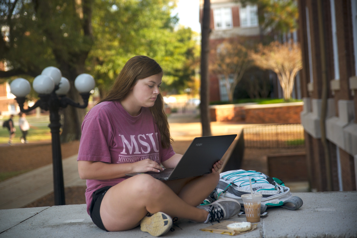 Female student studying with laptop outside Carpenter front stoop.