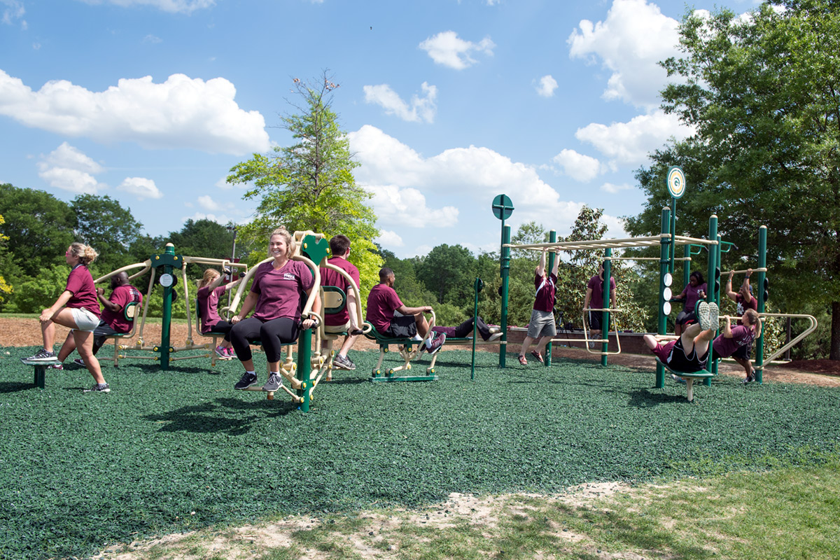 People wearing maroon using the new outdoor workout equipment near Chadwick Lake and Sanderson Center