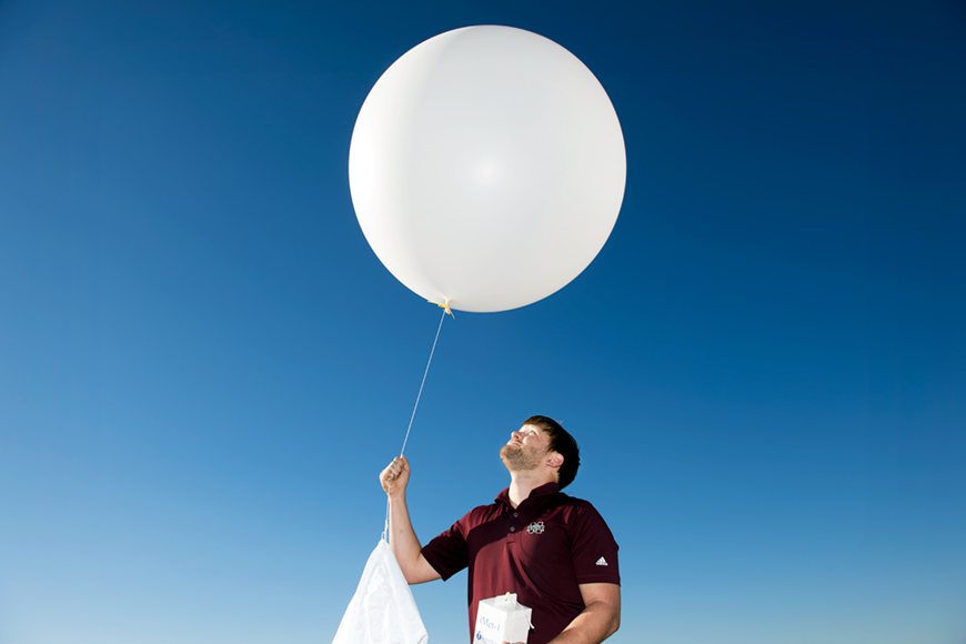 Barrett Gutter looks up at a white weather balloon he is holding.