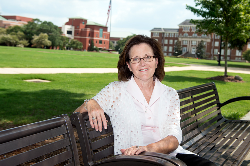 Teresa Jayroe sitting on a bench with the Drill Field in the background.