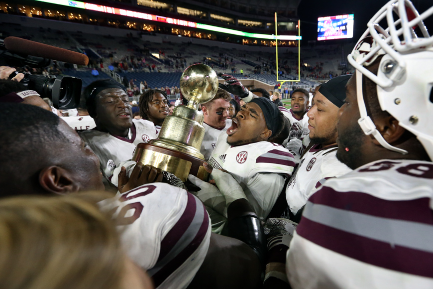 Football players celebrating Egg Bowl win and holding the Egg Bowl Trophy