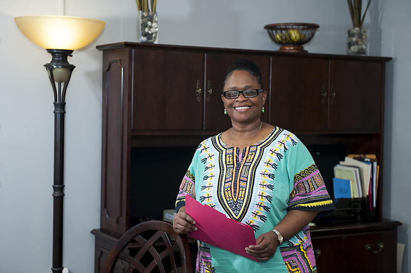 A photo of Dr. Dinetta Karriem standing by her desk in her office holding a folder, smiling.