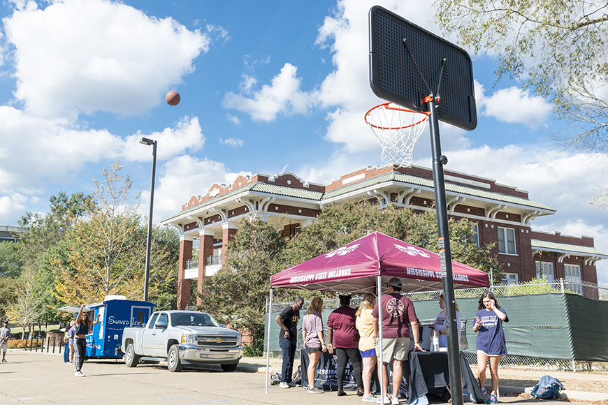 Student takes a long shot at a basketball hoop outside the YMCA building with booths in background during the MSU Student Association&amp;#039;s Shots for Tots fundraiser 