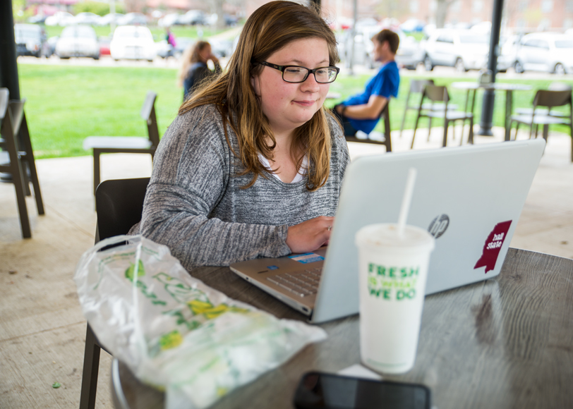 Katie Williams sits at a table outside, using her laptop to study for an upcoming test.