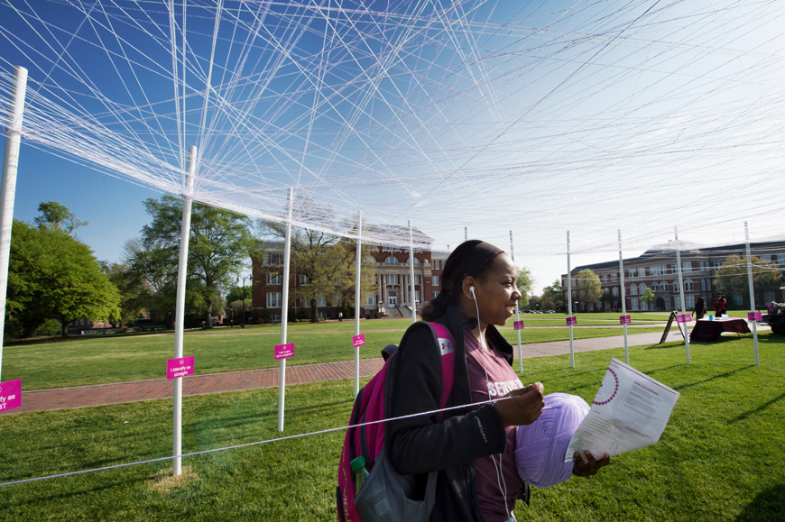 Student Essence Briggs stretches yarn between the identity posts of the UNITY Project public art on the Drill Field.