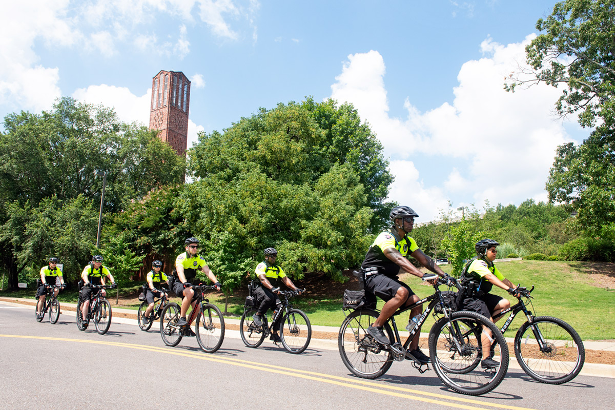 Eight campus police officers riding on bicycles in reflective neon near the carillon bell tower