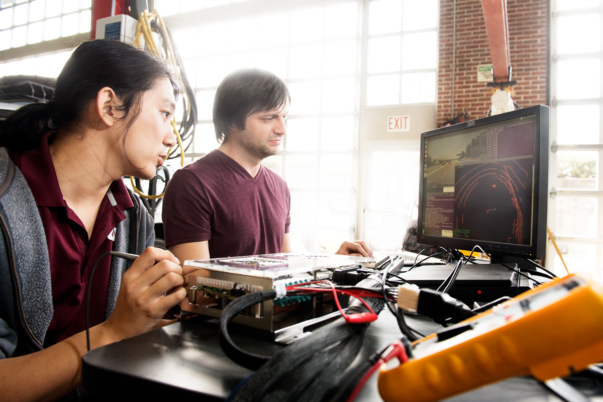 Two engineering students working on hard drive and simulation components for autonomous car.