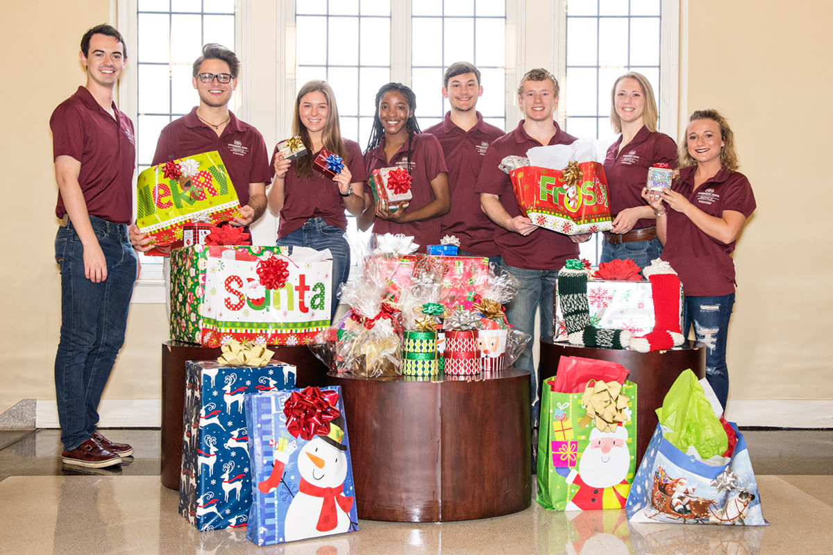 Students in maroon polos with gifts wrapped in colorful paper