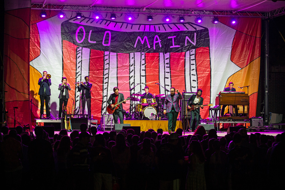 Musicians on stage with purple lights and backdrop saying Old Main.
