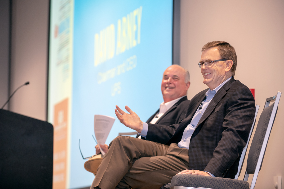 Two men in blazers on stage laughing while talking to attendees of conference