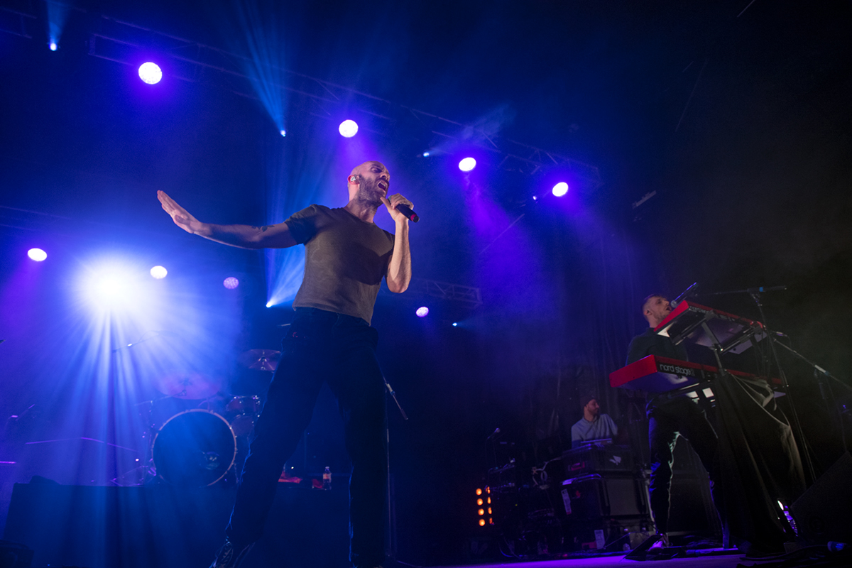 Singer with microphone on stage with purple lights surrounding him