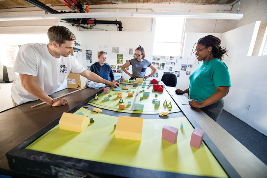 Four architecture students in Giles Hall architecture studio demonstrate interactive community design model they built for residents of Eastmoor Estates
