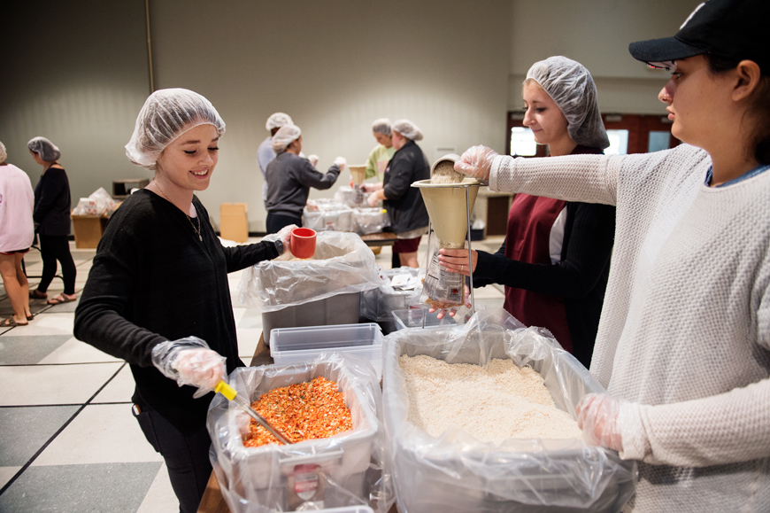 Students wearing food-safety hairnets work together as a team to fill rice, lentils and flavoring into packets during Stop Hunger now meal packing program.