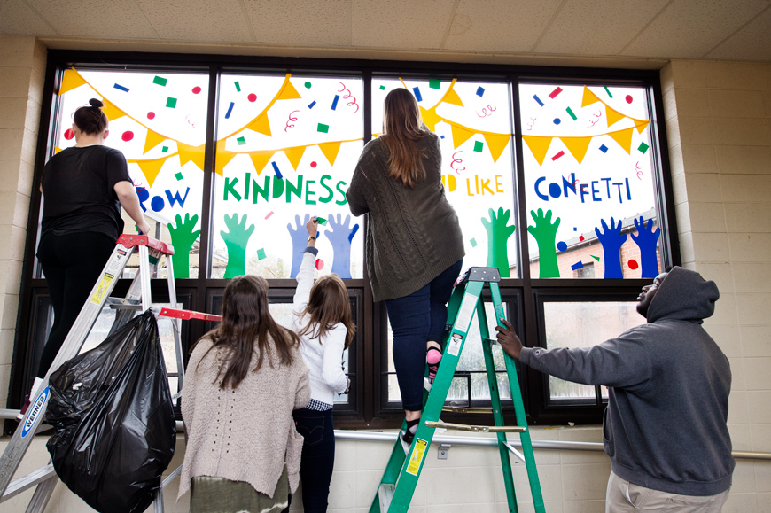Five art students apply graphic window stickers to windows at Sudduth Elementary school as final class project and outreach.