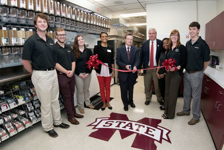 Nine people pose for a ribbon cutting photo at the College of Veterinary Medicine with animal food dispensers