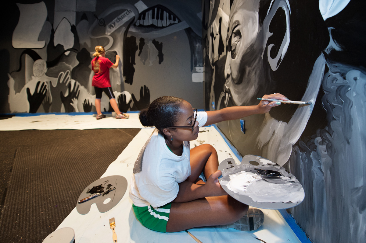 Two art students paint a music-themed mural on the walls of the Dawg House stage.