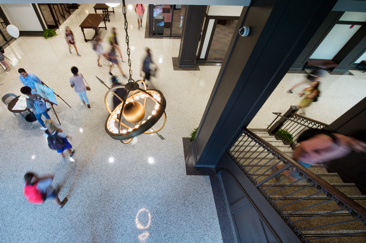 View looking down on swirl of students from Old Main Academic Center stairs, with hanging lantern with arrow at center.