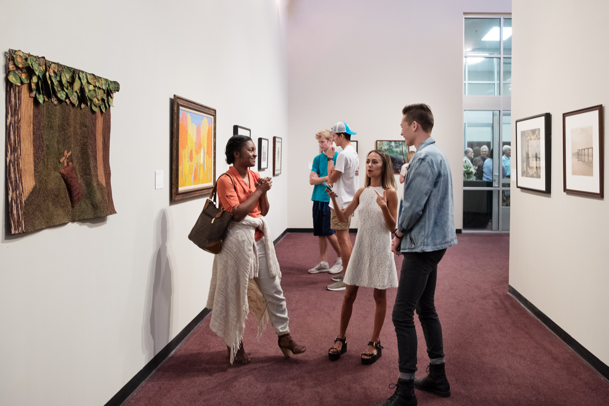 Three students chat in the Cullis Wade Depot Art Gallery, surrounded by art from the Mississippi Museum of Art&amp;#039;s collection.
