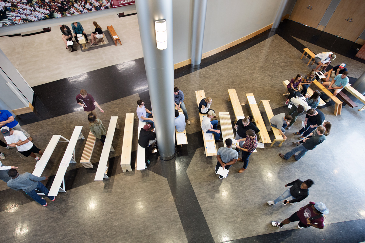 Viewed from above, dozens of benches are lined up with architecture students and professors talking and sitting amongst them.