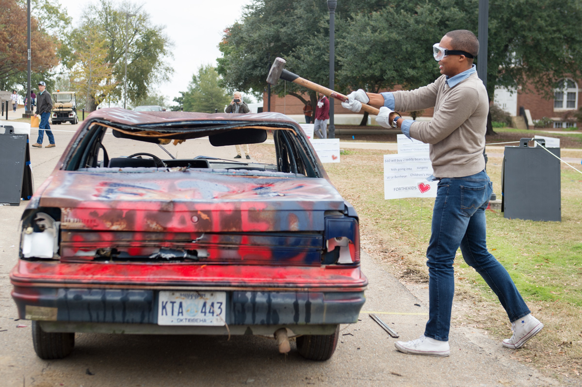 Student strikes an old car with a sledgehammer as part of MSU Dance Marathon fundraiser.