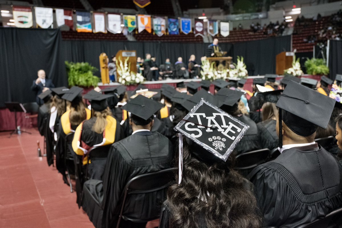 With the graduation stage in the background, a graduating student&amp;#039;s mortar board is decorated with &amp;quot;State&amp;quot; and a pawprint.
