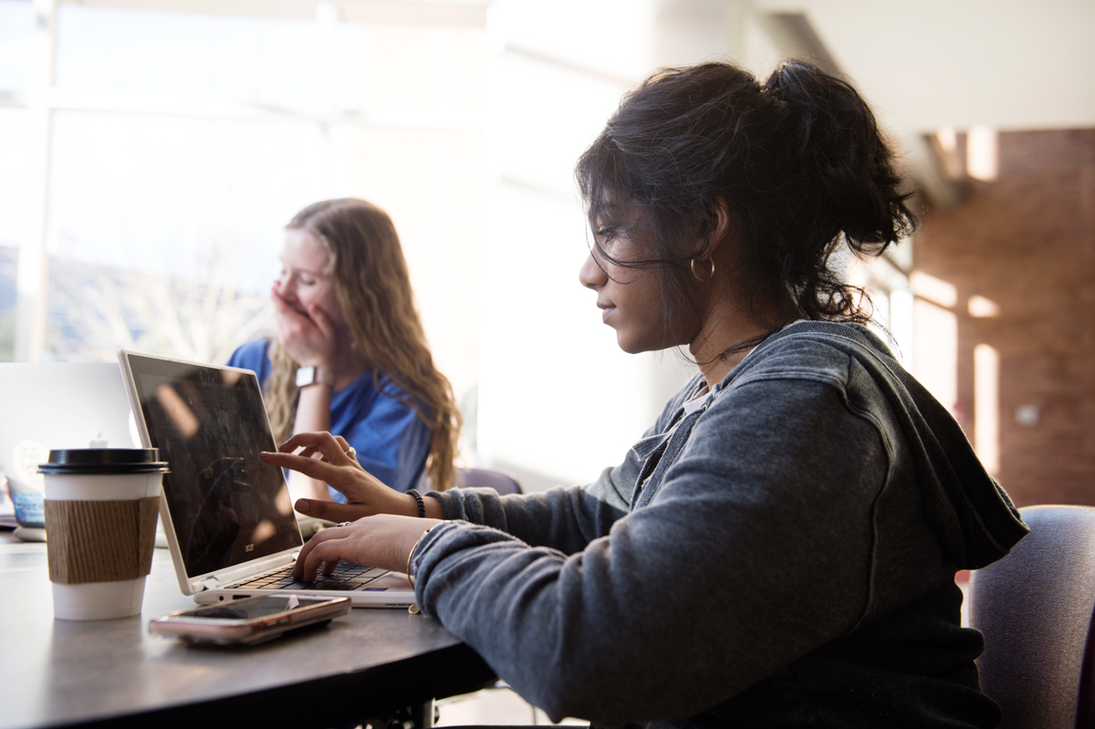 Emily Michael works on class assignments at a McCool atrium table while her friend Hannah Hederman laughs in the background.