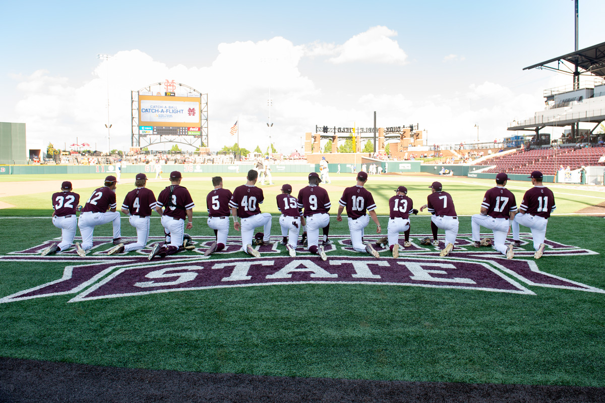 The Baseball team kneels on top of the Mississippi State logo on the side of Dudy Noble, watching Florida players warm up.