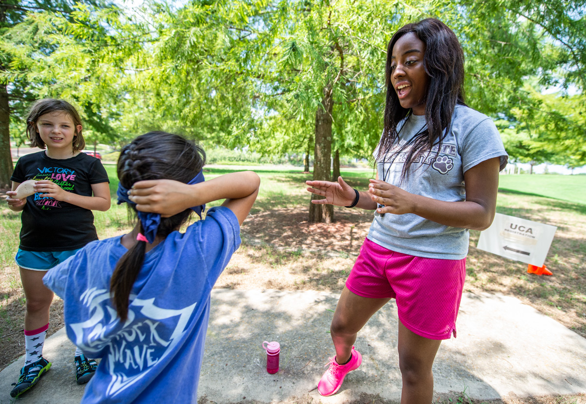 MSU student counselor Demi Wilkins directs two girl campers through a team building exercise outside.