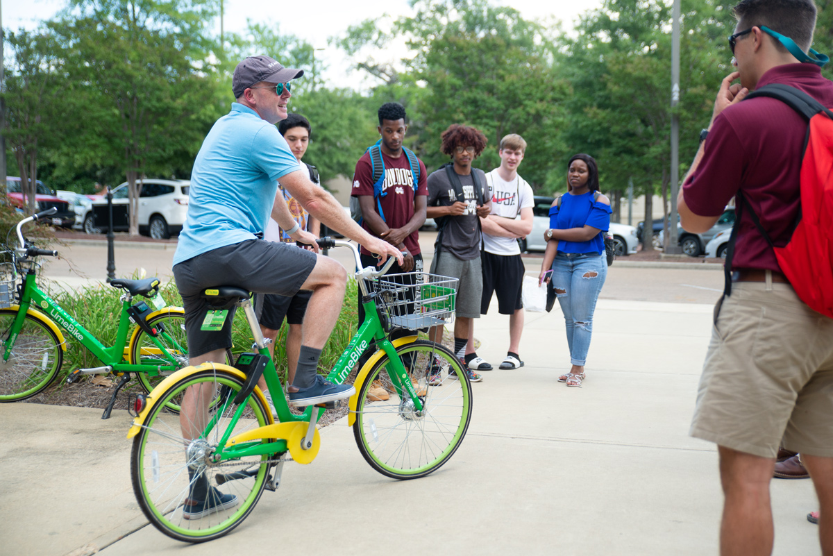 Professor Michael Seymour demonstrates riding a LIME Bike to his surrounding Bike to the Future students. 