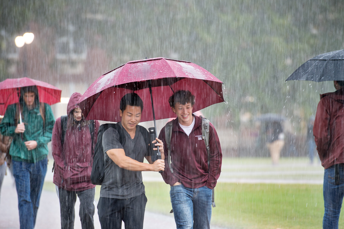 Students share an umbrella and a laugh as they cross the Drill Field in the pelting rain.