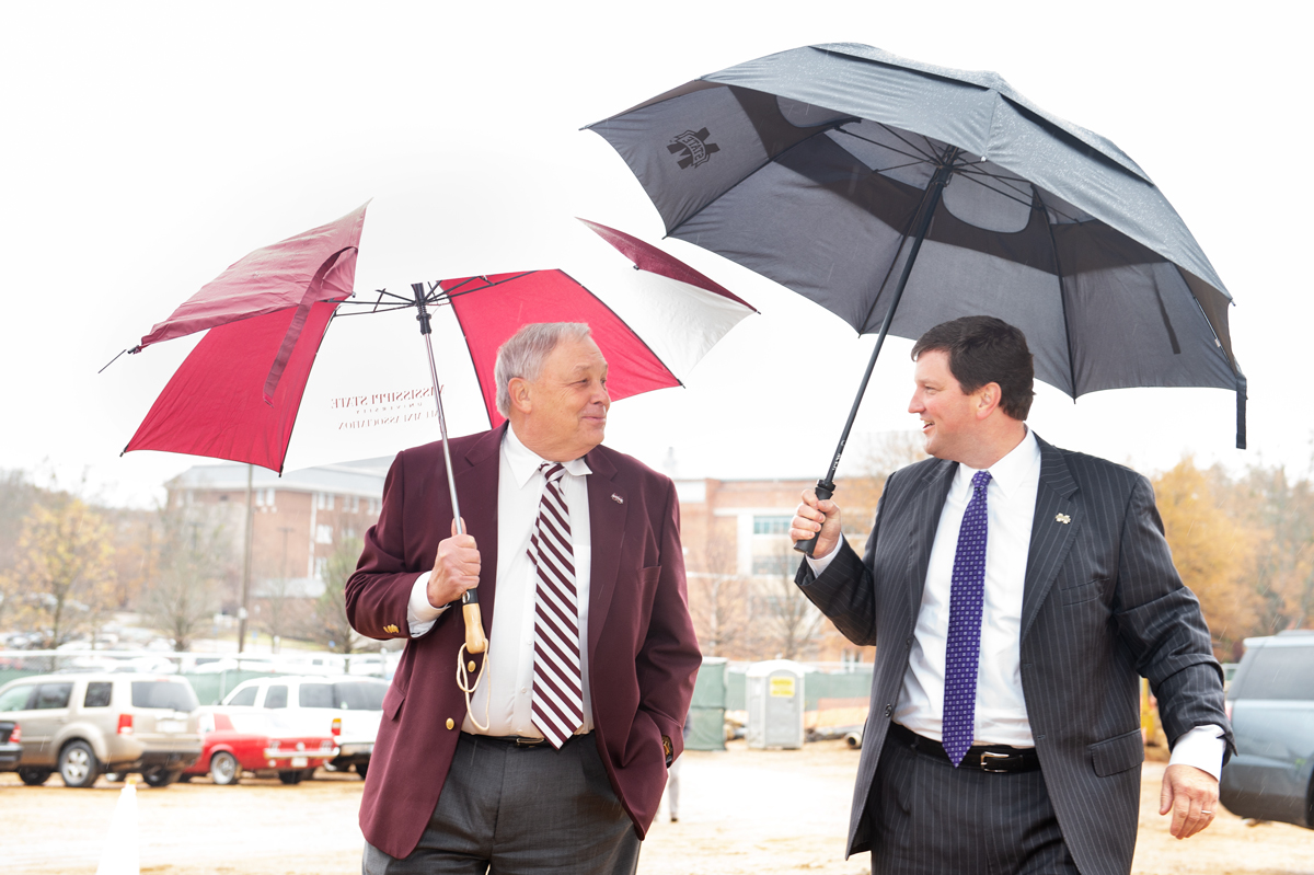Richard Rula and John Rush walk under umbrellas towards the Rula groundbreaking ceremony.