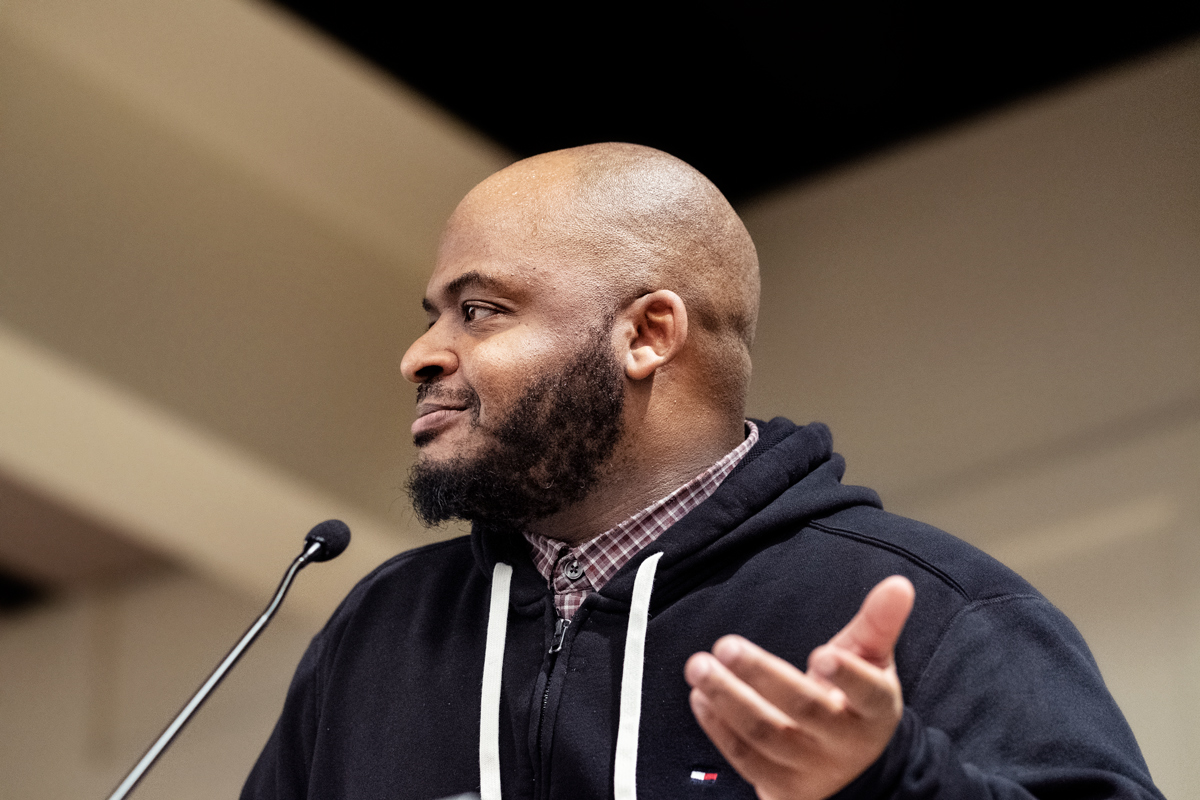 Black History Month keynote, Kiese Laymon, speaks at the podium microphone, looking out towards the audience.