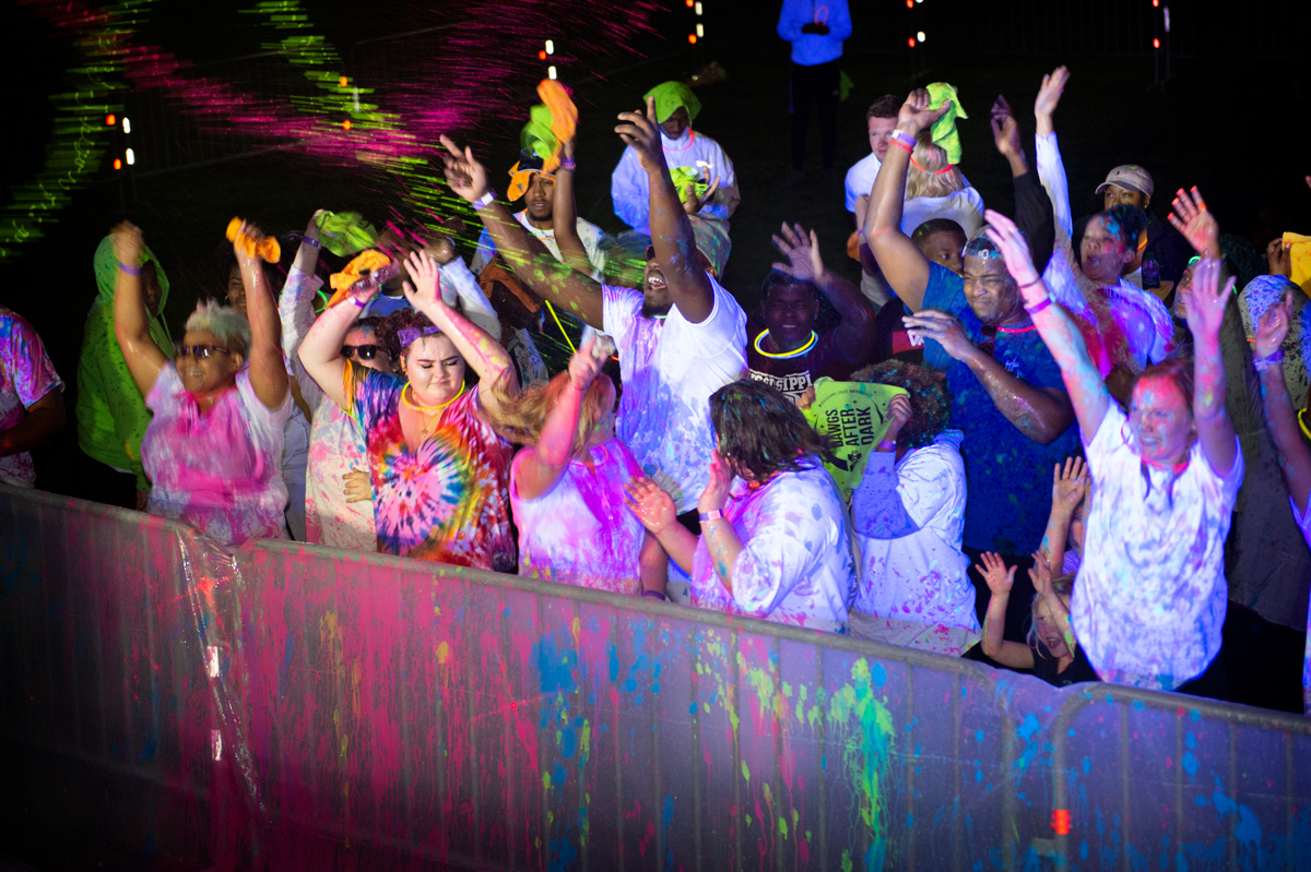 Students dance under glowing disco and black lights while being sprayed with flourescent paint.