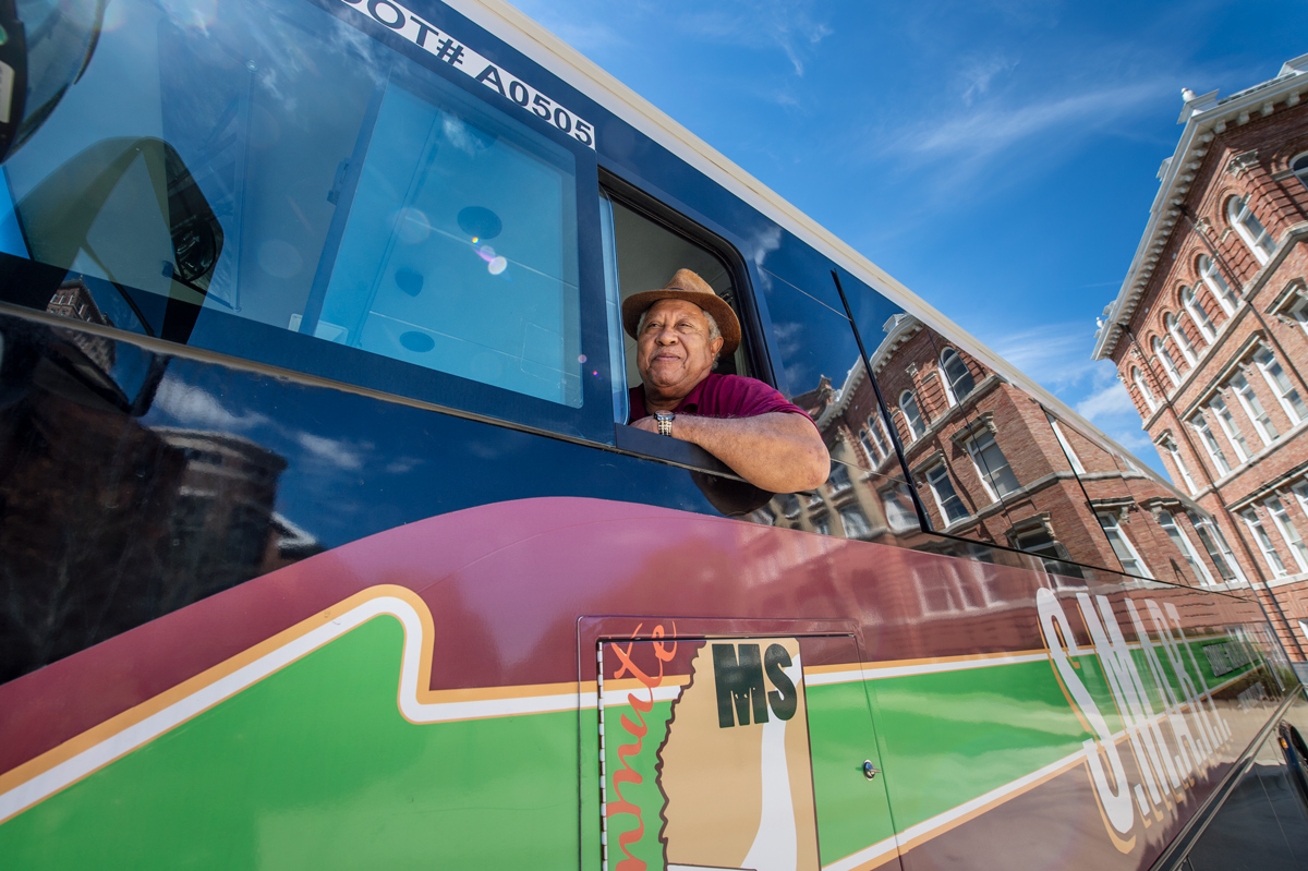 SMART Shuttle bus driver Ossie James framed in the window of the shuttle bus, with Montgomery Hall in the background.