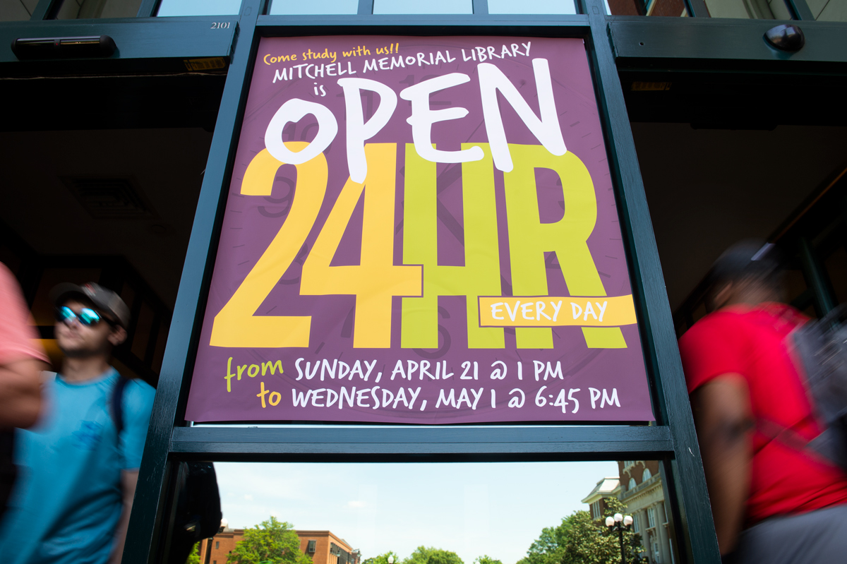 Michell Memorial Libraries &amp;quot;Open 24 Hours&amp;quot; hangs between its front doors as students pass through either side with motion blur.