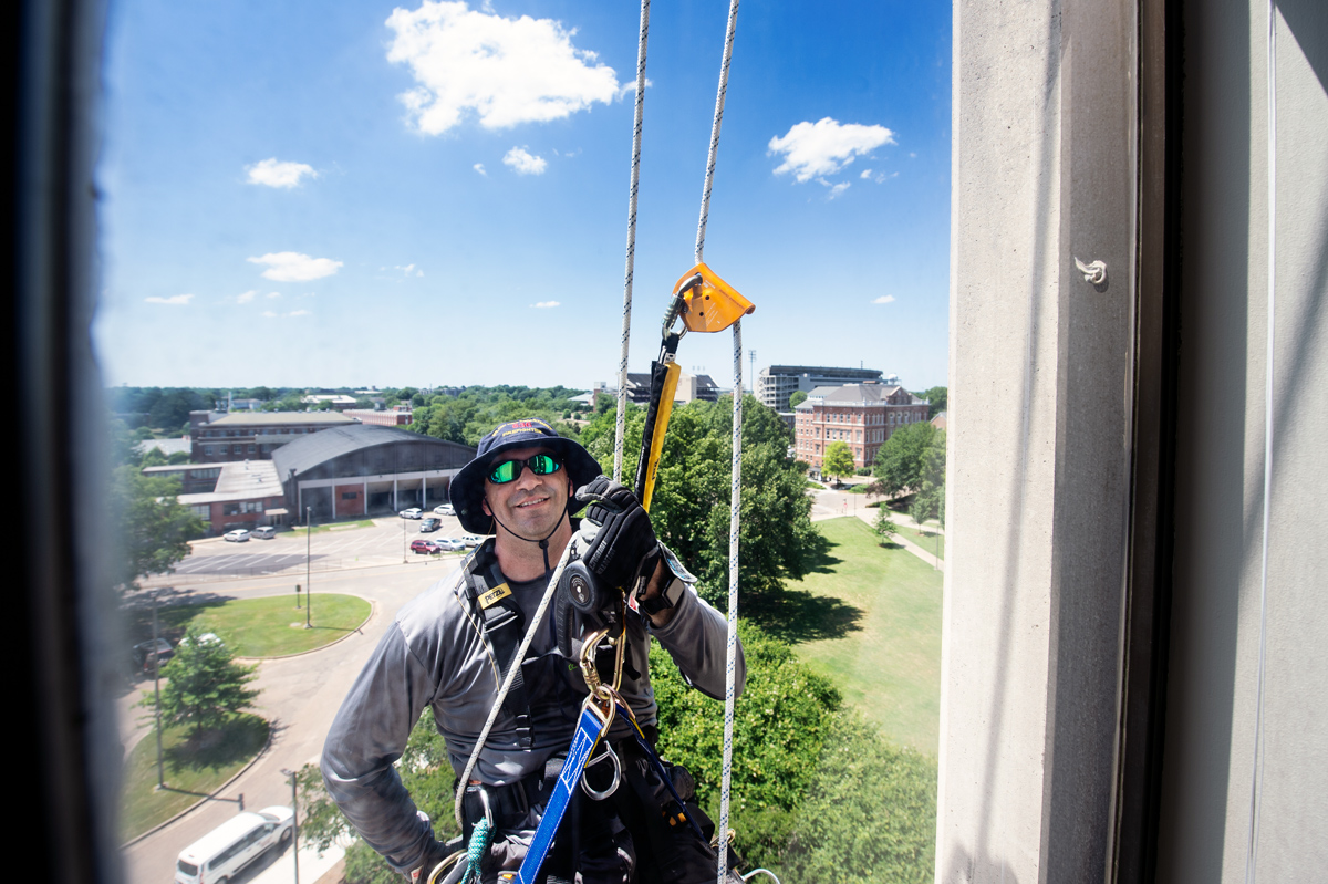 Building cleaner Anthony Frontiero swings past a 6th Floor Allen Hall window as he rappels past while cleaning the exterior.