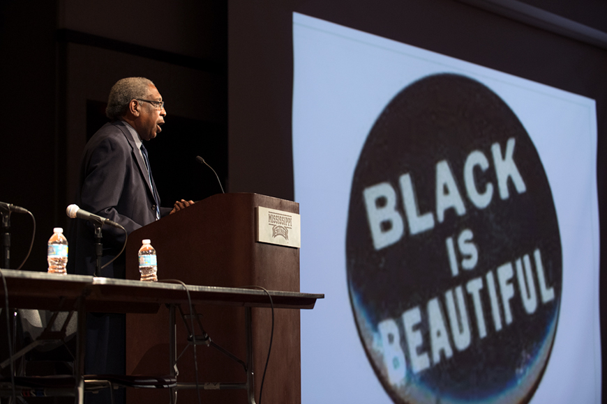 Speaker at podium with slide of &amp;quot;Black is Beautiful&amp;quot; in the background