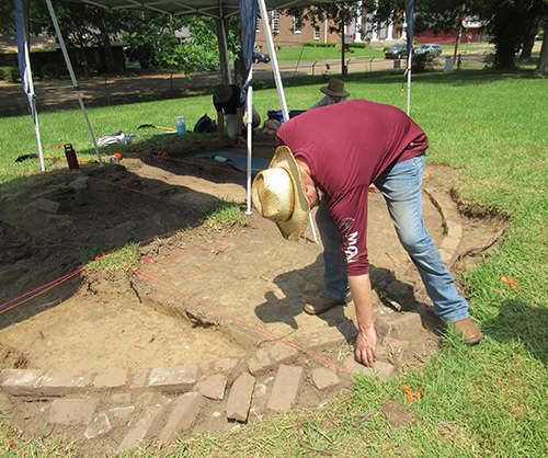 Jarod Duke, 5th year anthropology student at MSU, places his fingers in the fingerprint-shaped depressions in a brick from the 17 ft wide cistern