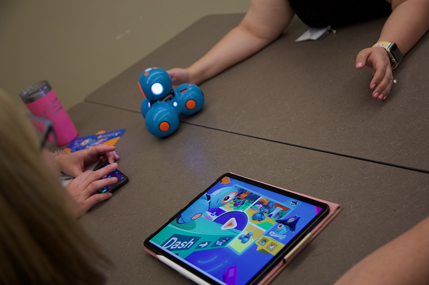 A robot is controlled by a tablet as teachers practice using it on a table.
