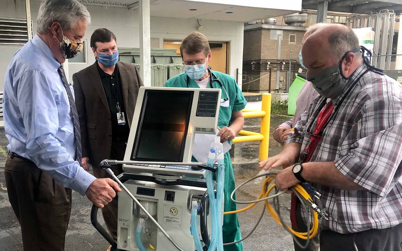 Four men unload one of two ventilators the university is loaning to the hospital