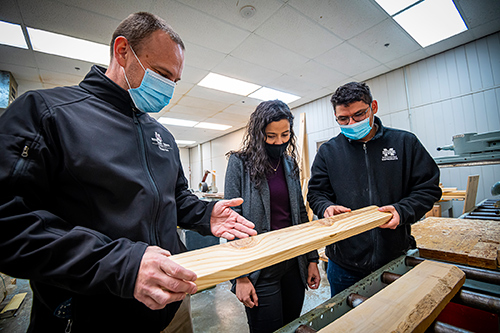 Rubin Shmulsky, professor and head; Gabrielly Dos Santos Bobadilha, postdoctoral associate; and Dercilio Junior Lopes, assistant research professor, all in the Department of Sustainable Bioproducts in MSU’s College of Forest Resources, examine defects in a piece of lumber. 