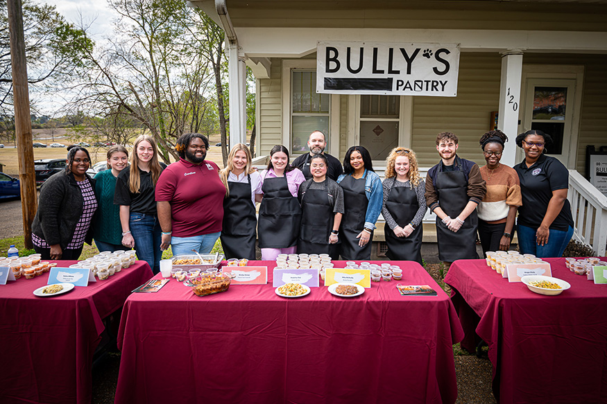 Volunteers gather around a table of food in front of Bully's Food Pantry
