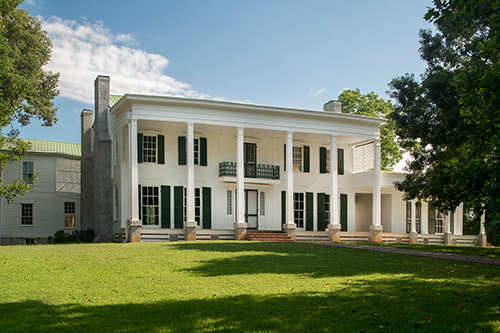 A large white antebellum two-story home with columns and green grass in the front yard