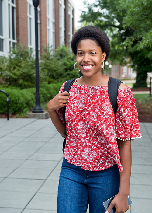 Donielle Allen smiles while standing on the sidewalk next to Colvard Student Union.