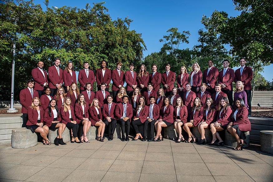 Forth-five students pose in rows wearing maroon coats outside.