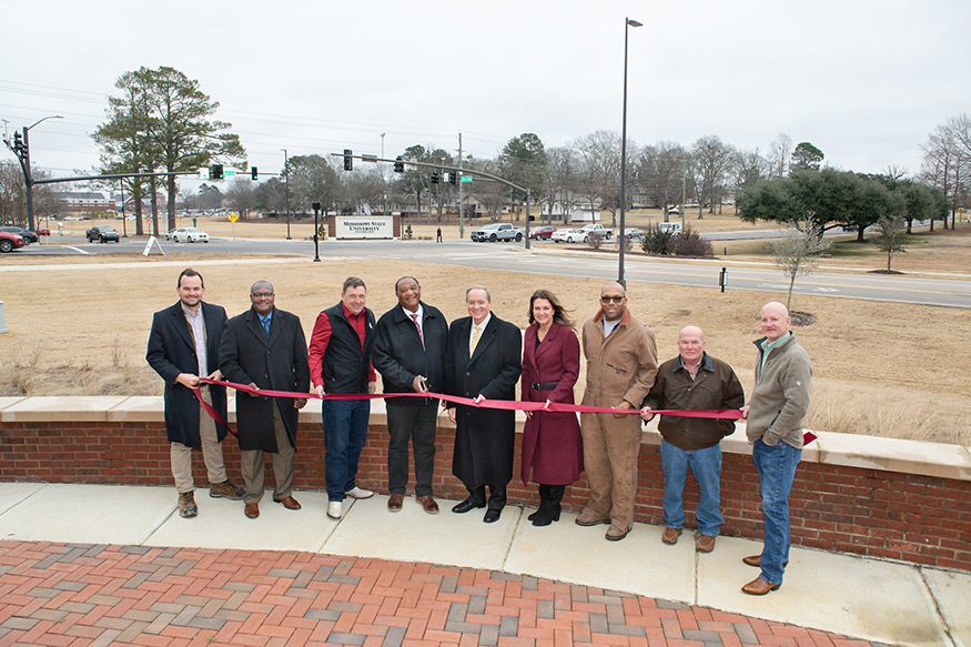 A group of campus and local officials cut a ribbon with Blackjack Road in the background